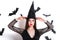 Happy gothic young woman in witch halloween costume with hat standing and smiling over white background