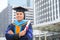 Happy graduate. Happy Asain man in graduation gowns holding diploma in hand on urban city background