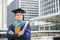 Happy graduate. Happy Asain man in graduation gowns holding diploma in hand on urban city background