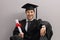 Happy graduate student with diploma leaning against gray wall