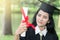 Happy graduate young Asian woman in cap and gown holding a certificated in hand, A diploma with red ribbon education concept in