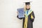 Happy graduated female student wearing graduation gown holds a d