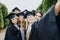 Happy graduates wearing caps and gowns celebrating in a park. Taking selfies and creating memories with faculty