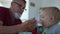 Happy grandfather feeding liquid food to grandson. Cute adorable toddler eating food with senior man. Funny little boy