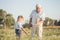 Happy grandfather and grandson walking at summer meadow.  Cute boy gives flowers his old grandpa