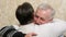 Happy gray-haired father is glad to meet s with adult son, hugging at home. Family joyful meeting. Son hugged his father