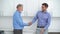 Happy gray-haired senior handsome male and cheerful young man in matching shirts handshake together in medical clinic