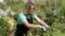 Happy greenhouse female owner cutting houseplants with pruner