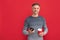 happy grizzled guy in sweater drink coffee with smartphone on red background with copy space, chat