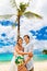 Happy groom and bride having fun on the sandy tropical beach under the palm tree. Wedding and honeymoon concept.