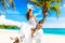 Happy groom and bride having fun on the sandy tropical beach under the palm tree. Wedding and honeymoon concept.
