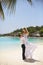 Happy groom holds bride on his hands under wedding ceremony arch on tropical island beach on Maldives. Turquoise ocean