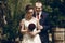 Happy groom hugging beautiful bride in white wedding dress and red flowers bouquet from behind, happy newlywed couple moment