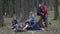 Happy group of friends camping in the woods enjoying nature playing guitar and singing together lying down the grass -