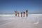 Happy group of friends jumping together on beach in the sunshine