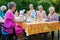 Happy group of senior ladies enjoying art class seated around a table outdoors in the garden painting with water colors while
