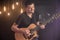 Happy guitarist in a black t-shirt plays an acoustic guitar at a concert against a blurred black background. Close up