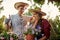 Happy guy and girl gardeners in a straw hats hold pots with petunia on the garden path in  on a sunny day.