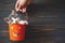 Happy Halloween. Cute kitten sitting in halloween trick or treat bucket on black wooden background. Hand holding jack o` lantern