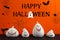 Happy Halloween greeting card design. White pumpkin shaped candle holders on table against orange background with