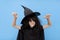 Happy Halloween kid raises his hands up while casting a spell. Child in black sorcerer's costume. Witch on blue