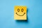 Happy hand drawn yellow color sticky note, smiling sticky note paper isolated in blue background.