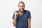 Happy handsome bearded guy with stylish hairstyle brightful smiling with teeth and pointing upside with finger on white