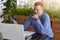 A happy handsome confident businessman with red hair dressed in checked shirt sitting at table in front of open laptop holding pie