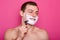 Happy handsome man shaving his face over rose background, prepares for dating, looking at mirror with charming smile, posing with