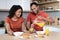 Happy handsome young black guy in red t-shirt pours juice into glass to his wife, couple enjoys breakfast