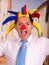 Happy handsome young businessman with a red clown nose and colorful harlequin hut in his head