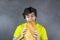 Happy handsome young teen boy holds and eats freshly baked bread. Hungry boy bites big loaf, on gray background