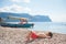 happy healthy dreaming little child lying on summer sea beach with boat and rocky mountain on background