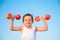 Happy healthy little caucasian boy lifting apple dumbbells on blue sky background with copy space