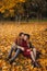 Happy heterosexual couple sits on the ground covered by yellow leaves on the autumn day. Handsome man and beautiful