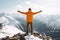 happy hiker celebrating success on the top of a mountain with raised arms, wearing an orange jacket, concept of overcoming a hard