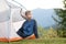 Happy hiker child boy resting in a tourist tent at mountain campsite enjoying view of beautiful summer nature
