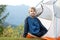 Happy hiker child boy resting in a tourist tent at mountain campsite enjoying view of beautiful summer nature