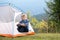 Happy hiker child boy resting in a tourist tent at mountain campsite enjoying view of beautiful summer nature