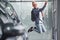 Happy hipster guy jumping indoors against grey background and near car