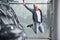 Happy hipster guy jumping indoors against grey background and near car