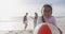 Happy hispanic girl holding ball on beach with family in background