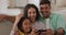 Happy hispanic parents and daughter sitting on sofa taking selfie