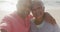 Happy hispanic senior couple embracing, taking selfie on beach at sunset