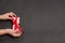 Happy Holidays concept with woman hands holding present box with red bow on pastel dark background . Flat lay style