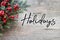 Happy Holidays Text with Christmas Evergreen Branches and Red Winter Holiday Berries in Corner Over Rustic Wooden Background