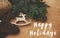 Happy Holidays text sign on reindeer toy, gloves, basket with fir branches and cones on rustic wooden background. Flat lay. Zero