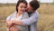 Happy husband tenderly embraces his pregnant wife standing in a field at sunset.