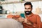 Happy Indian Bearded Guy Using Smartphone Texting At Home