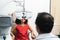 Happy Indian child girl doing eyes test with phoropter digital modern machine and ophthalmologist or optometrist